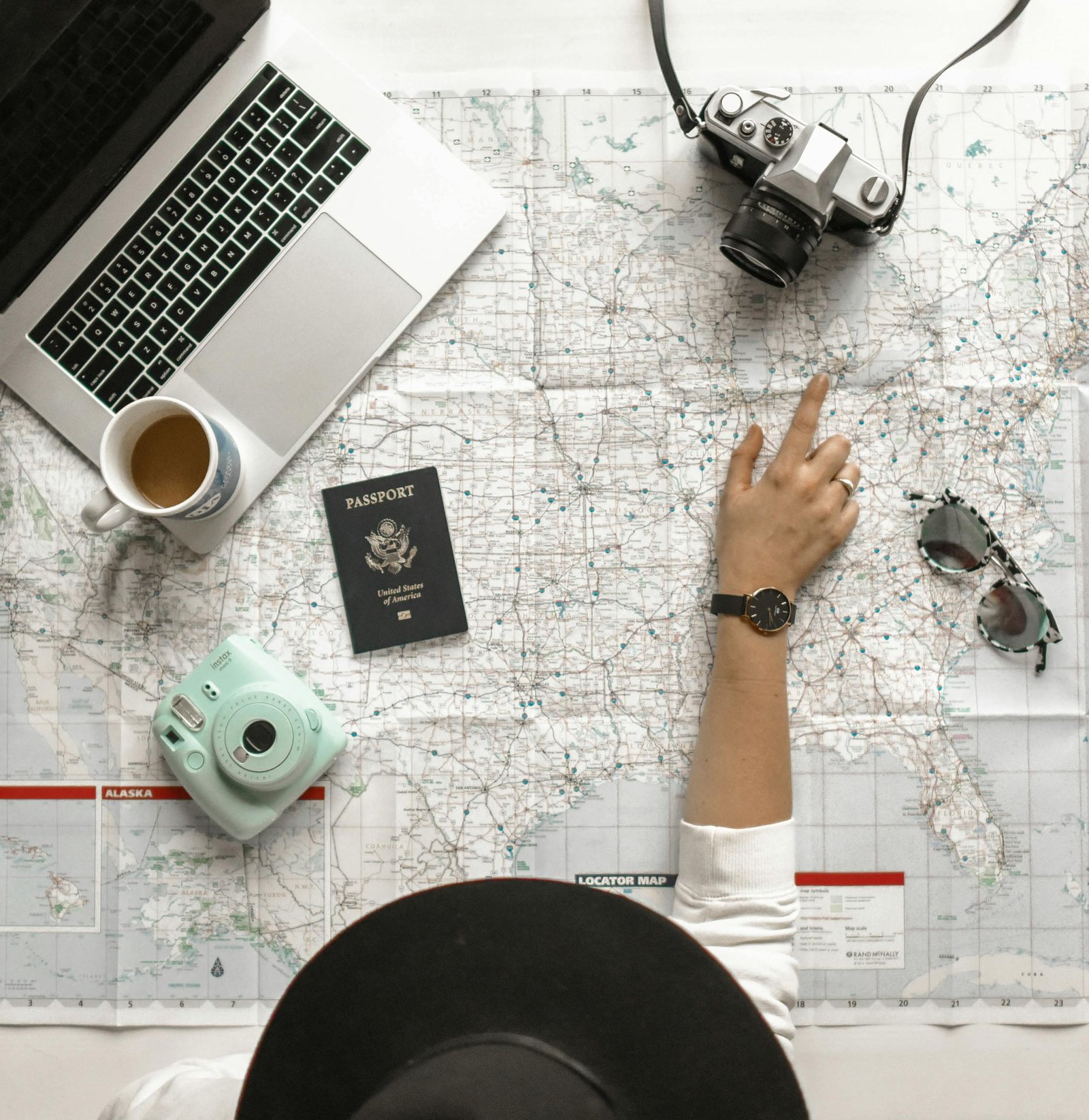 Hand on map with camera, passport, laptop, and coffee, perfect for travel planning inspiration.